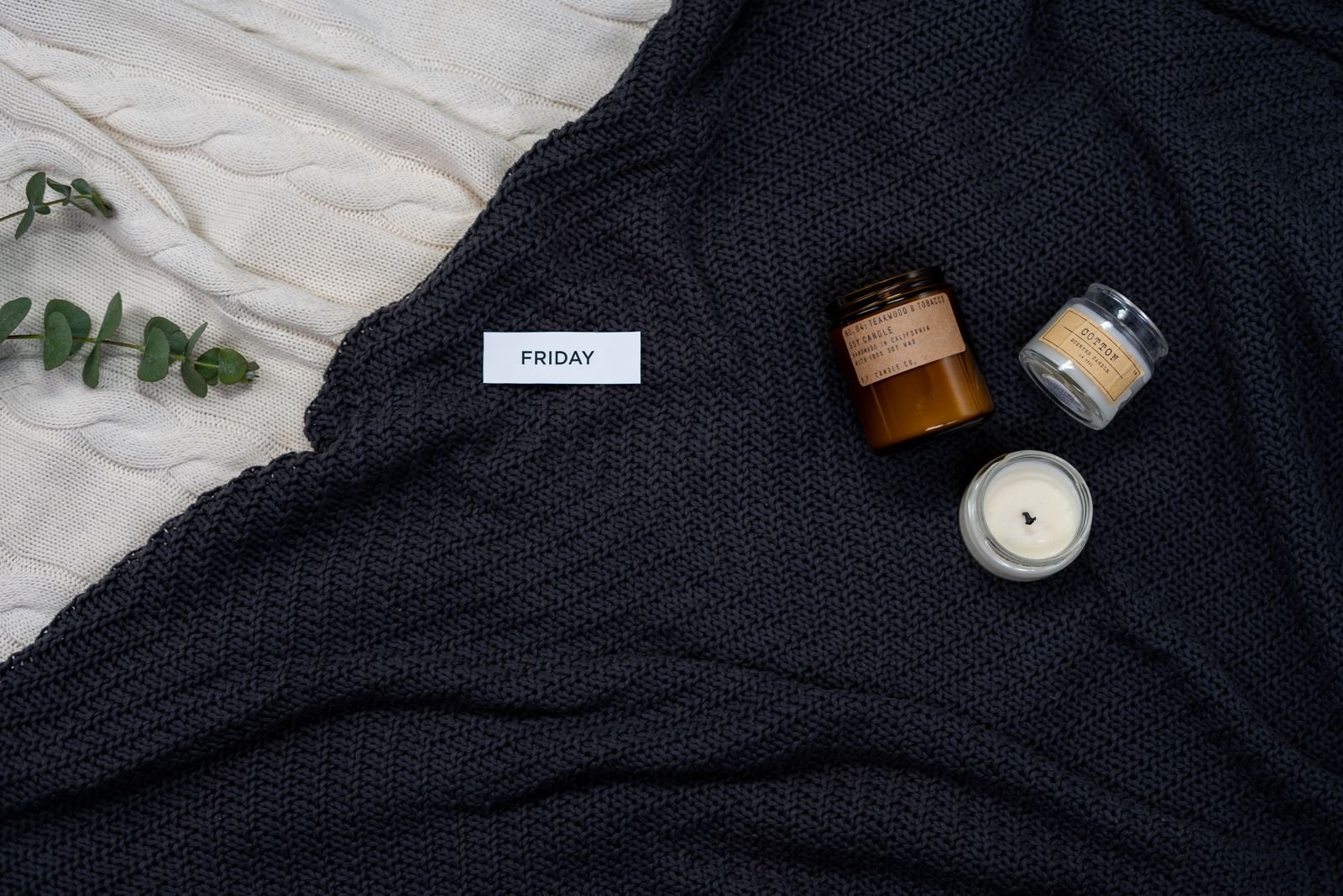 A chunky knitted blanket layered with lit candles and eucalyptus
